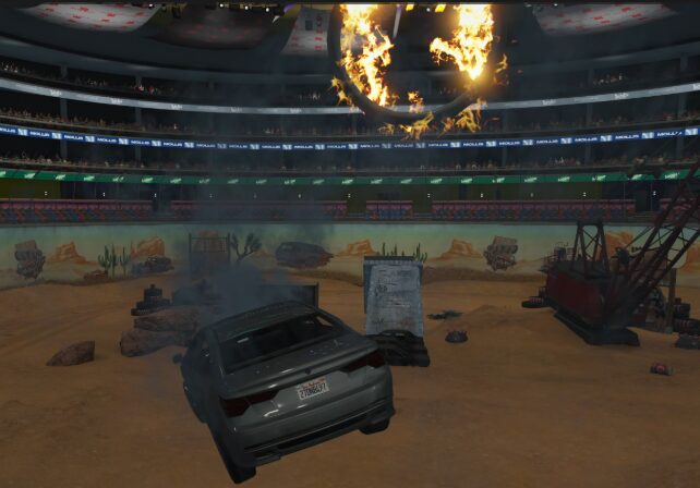 A wrecked car inside an extreme sports arena underneath a ring of fire.